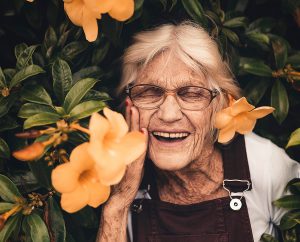 Photo of an old laughing woman amidst orange flowers