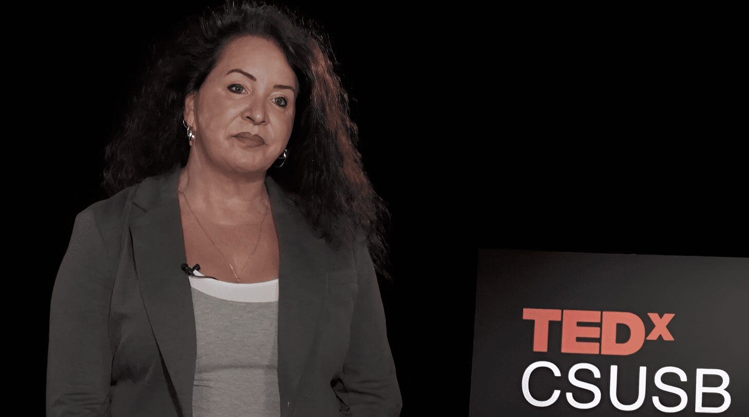 Woman speaking beside TEDx CSUSB sign