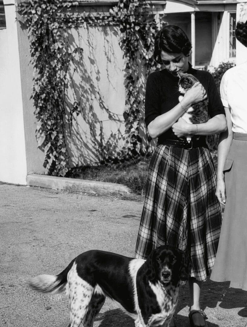 Lady cuddles kitten, dog stands close